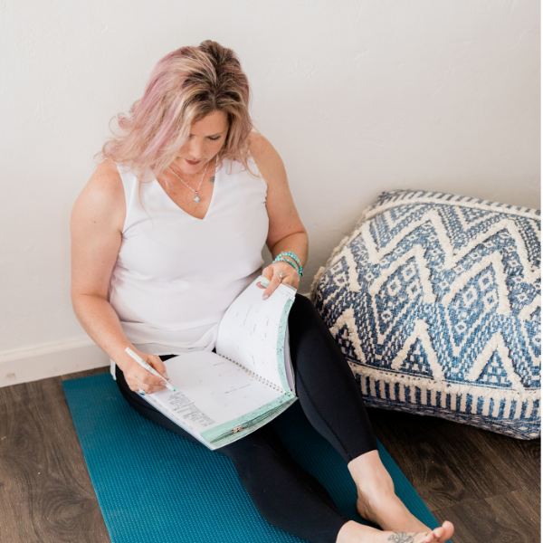 Women sitting on yoga mat writing out her goals in a journal